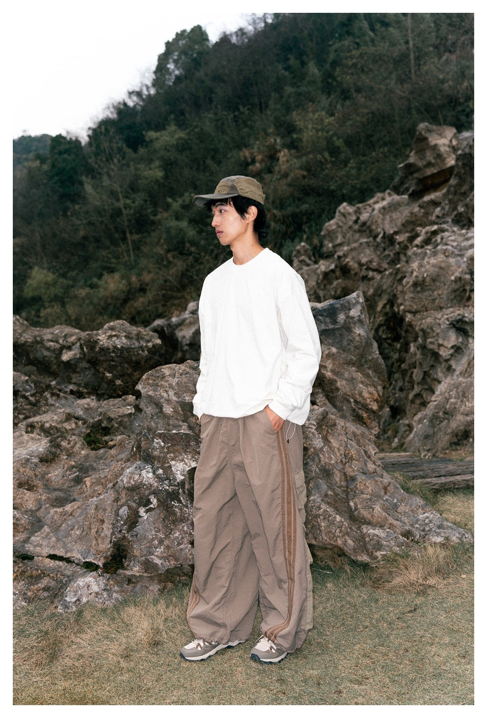 Side view of a model wearing a white long-sleeve shirt and loose taupe pants with brown side stripes.