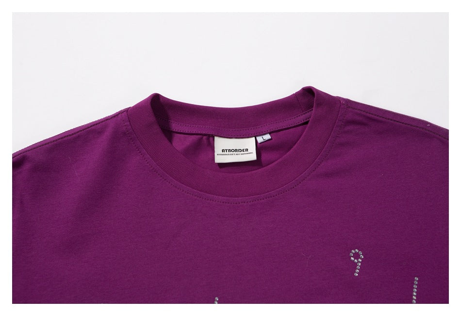 Close-up of the purple T-shirt's crew neckline, sewn neck label, and rhinestone chest detail.