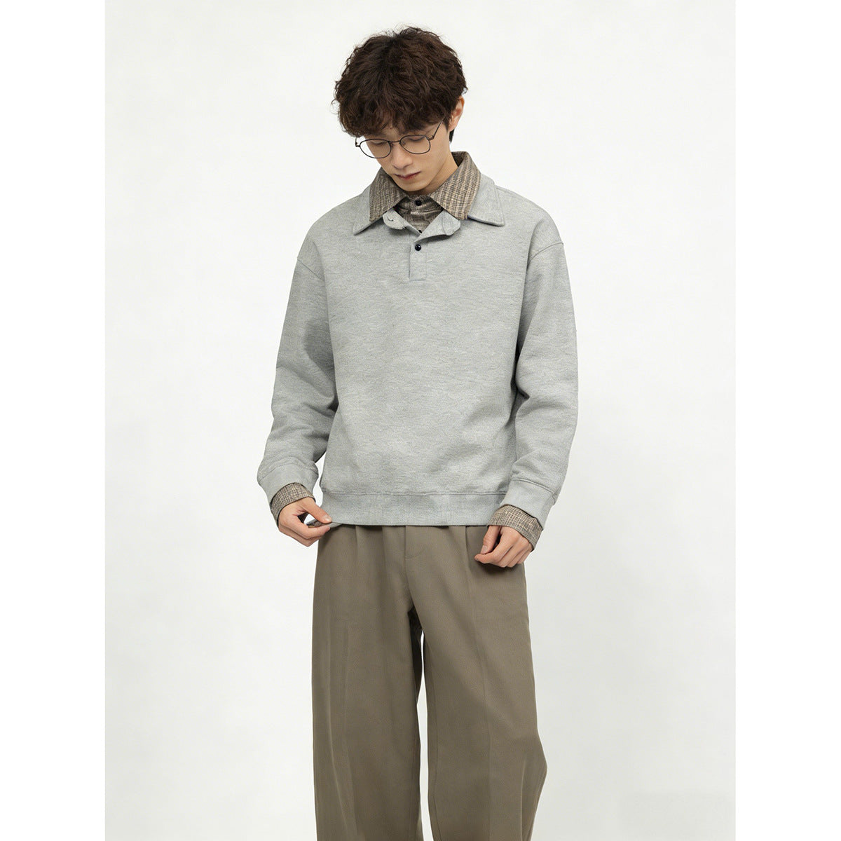 Model wearing a light gray collared pullover with plaid collar and cuffs, paired with loose taupe trousers.