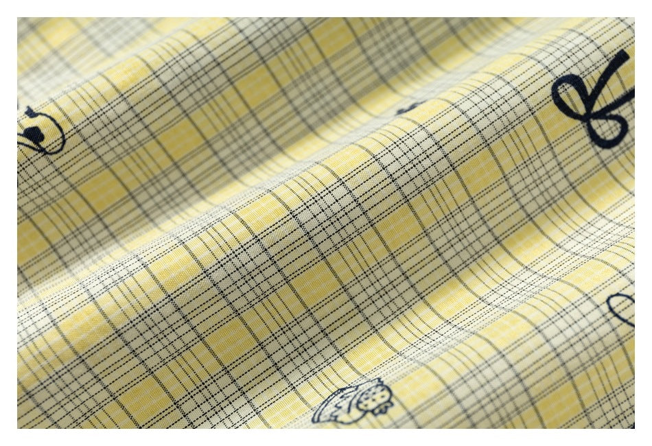 Close-up of yellow plaid fabric with fine dark grid lines and small navy dog and bow motifs.