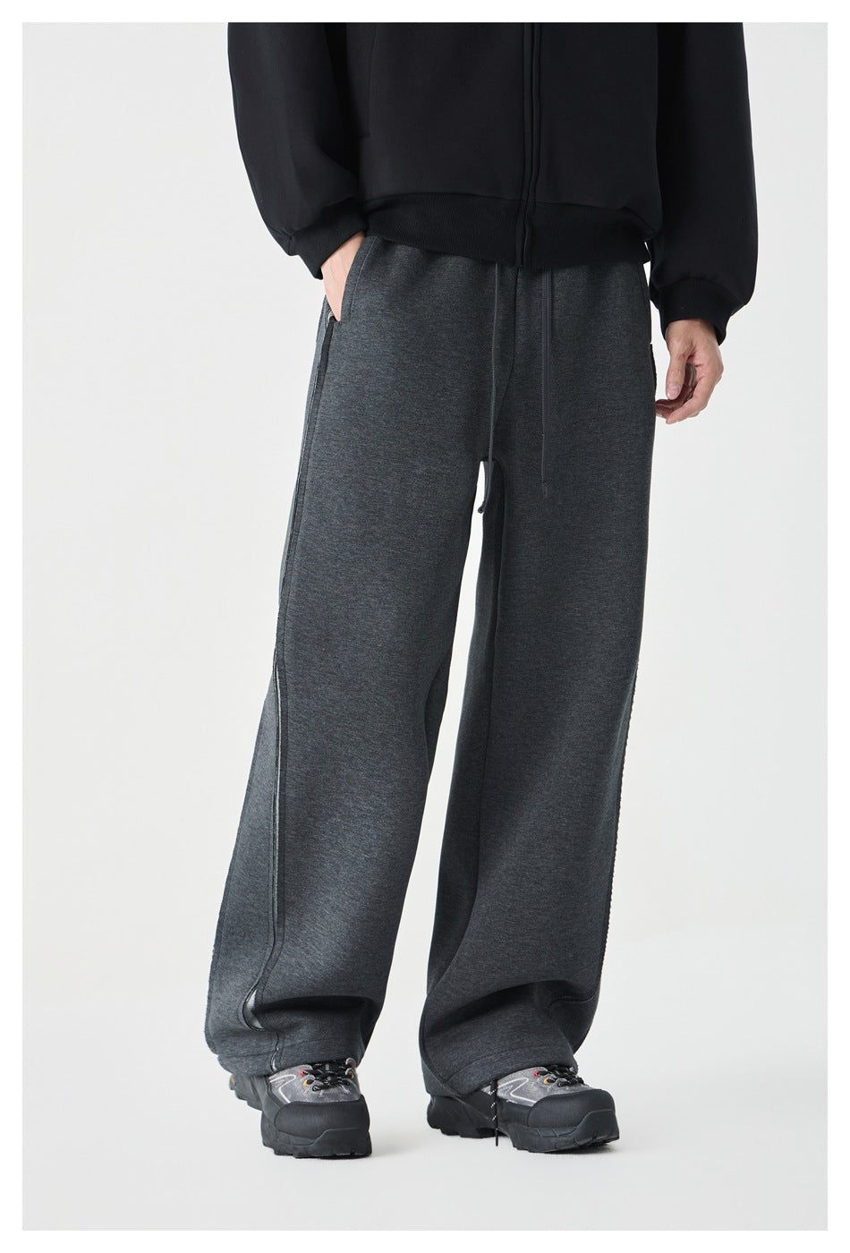 Front view of a model wearing loose charcoal sweatpants with a drawstring waist and long vertical seams.