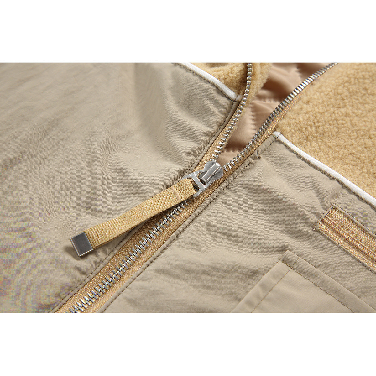 Close-up of the jacket's metal zipper, tan pull tab, beige panels, and white piping.