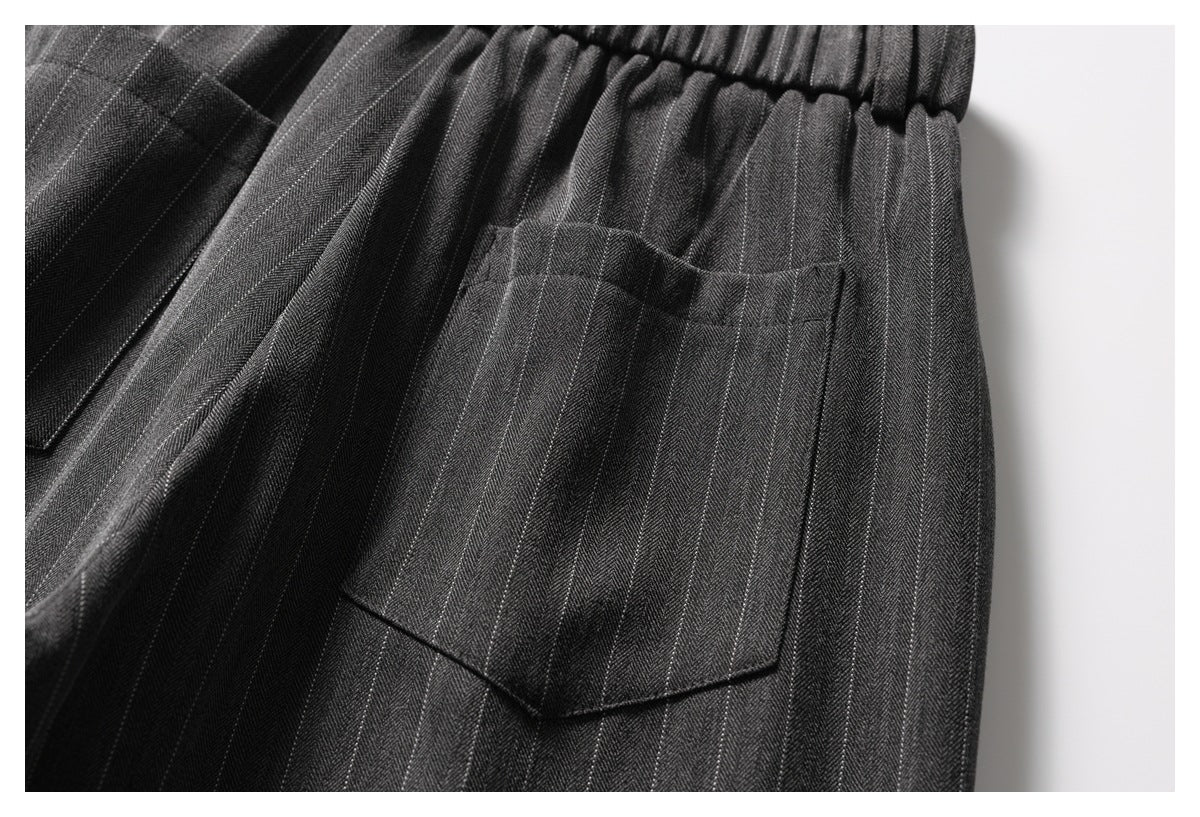 Close-up of charcoal pinstripe trousers showing an elasticated waistband and a large patch pocket.