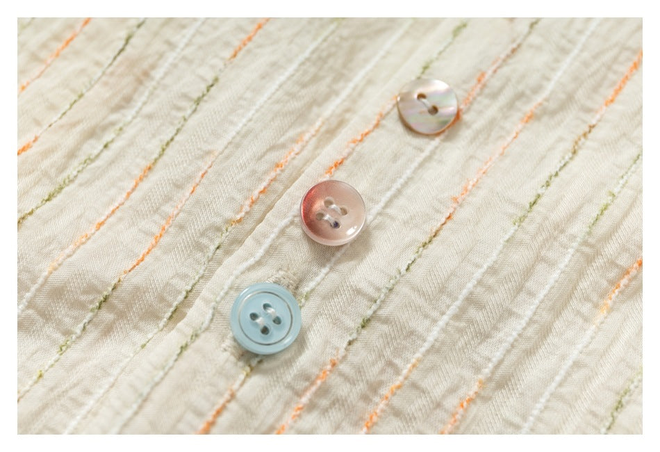 Close-up of an ivory shirt with raised orange and olive stripes and three pastel buttons.