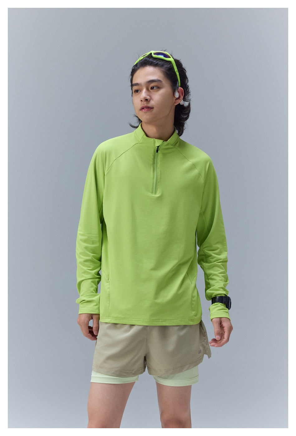 A man models a bright lime quarter-zip long-sleeve top with layered beige and pale green athletic shorts.