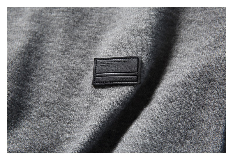 Close-up of a small black rectangular patch sewn onto heather gray knit fabric.