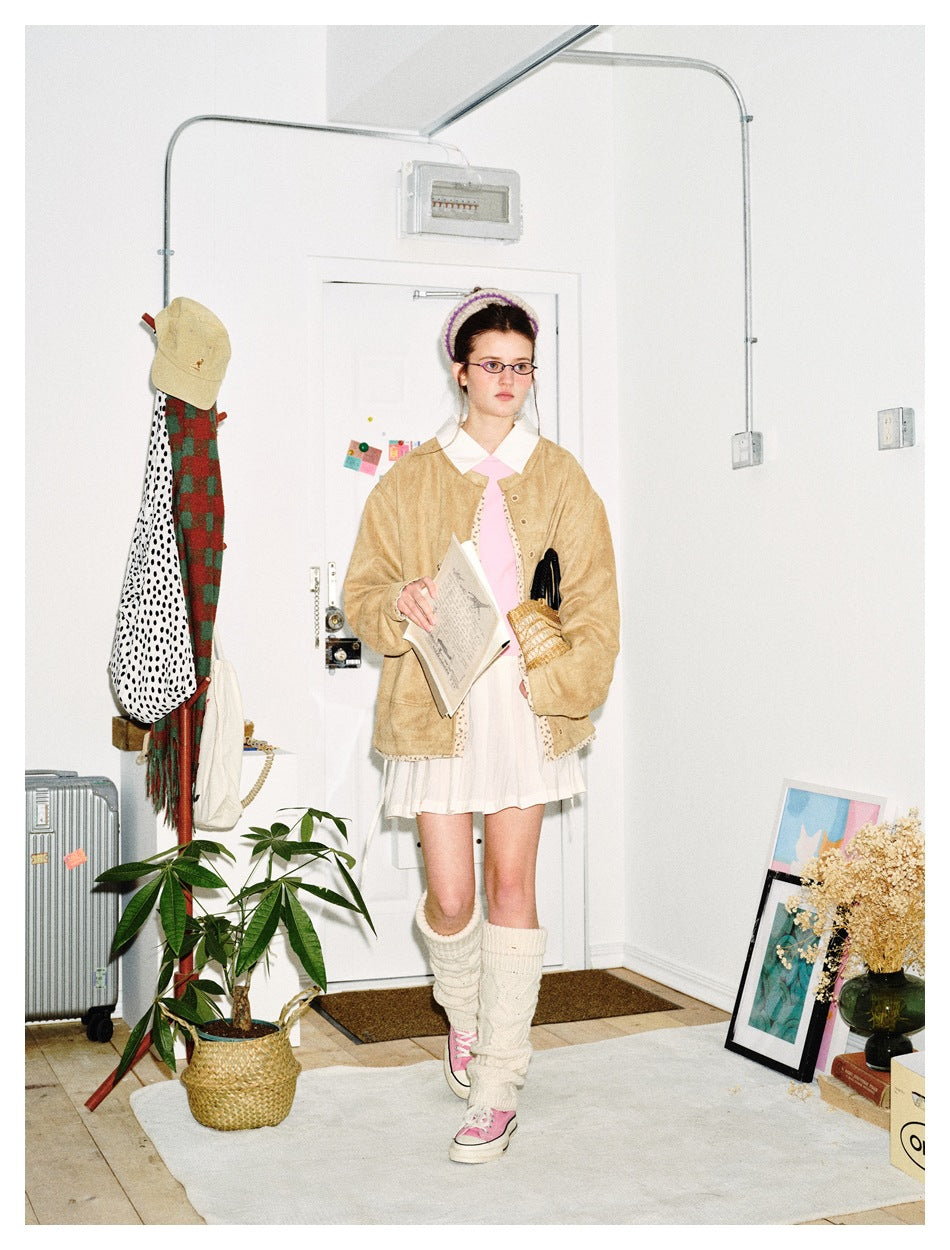 Front view of a model wearing a tan jacket with patterned trim over a white outfit and pink tie.