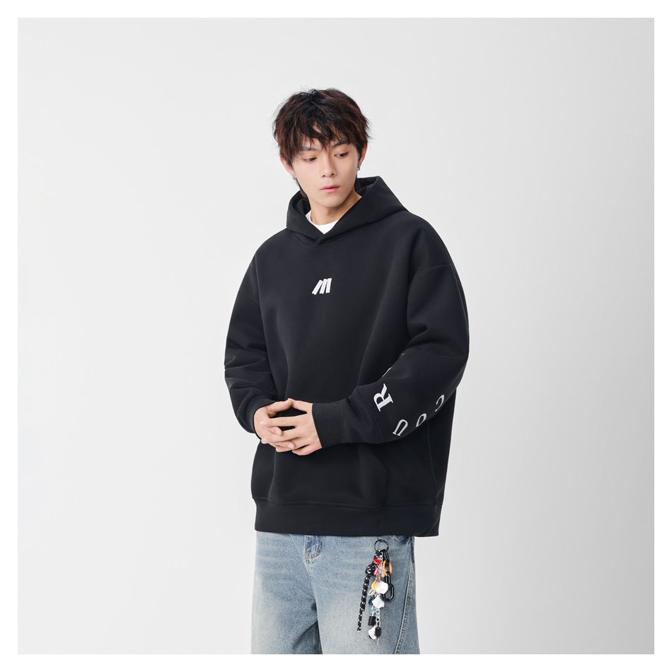 Model wearing a black oversized hoodie with white chest logo and sleeve lettering, with light blue jeans