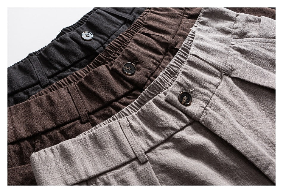 Close-up of black, dark brown, and light gray trousers arranged together, showing elastic waistbands, buttons, and belt