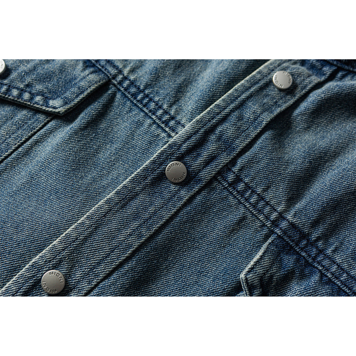 Close-up of a washed blue denim button placket with metal buttons and diagonal seams.