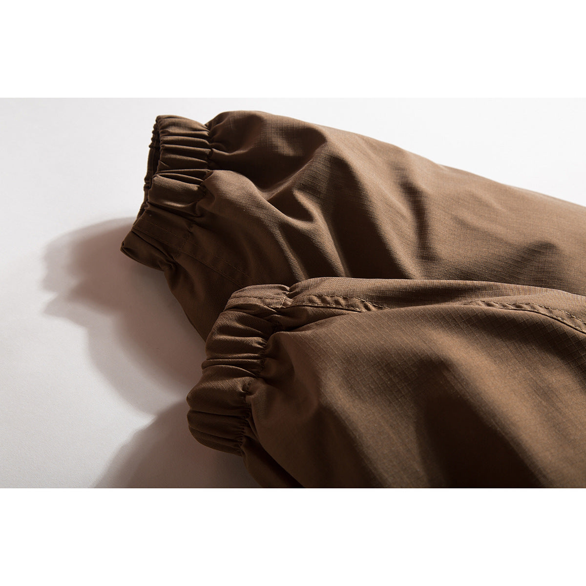 Close-up of brown jacket sleeves with gathered elastic cuffs and subtle grid-textured fabric.