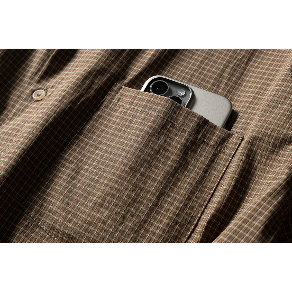 Close-up of the shirt's brown plaid chest pocket holding a smartphone.