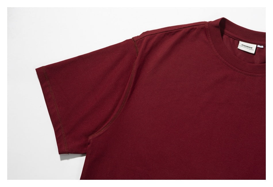 Close-up of a burgundy T-shirt's short sleeve, shoulder seam, and crew neckline on a white background.
