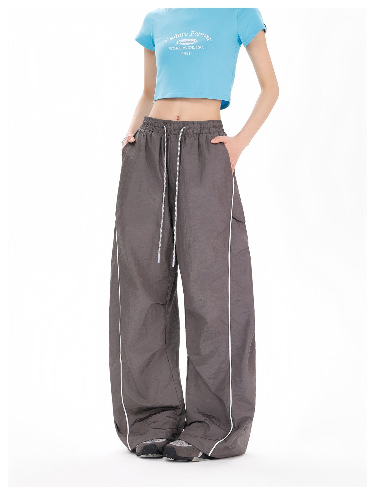 Front view of charcoal-gray wide-leg pants with a gathered drawstring waist, white piping and side pockets, worn by a model.