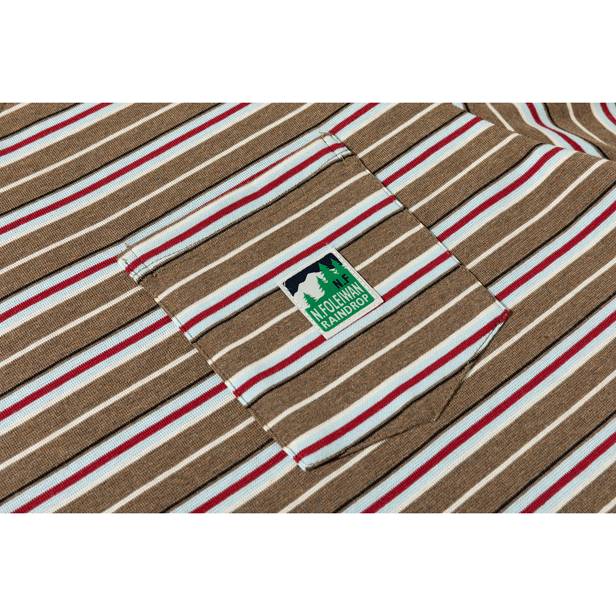 Close-up of a brown striped T-shirt's chest pocket and green sewn patch.