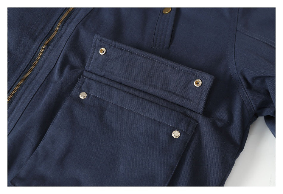 Close-up of a navy garment with layered snap-button pockets and a brass-colored zipper.