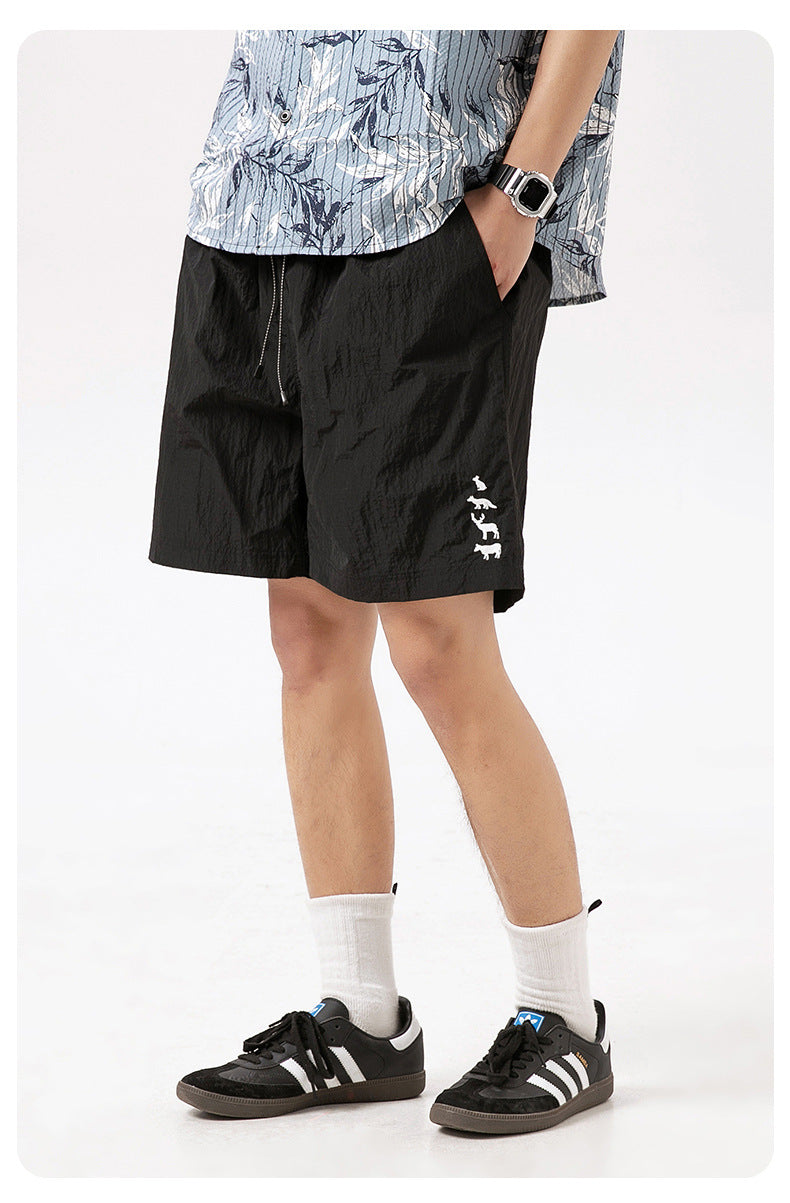 Model wearing black drawstring shorts with animal embroidery, a patterned short-sleeve shirt, white socks and sneakers