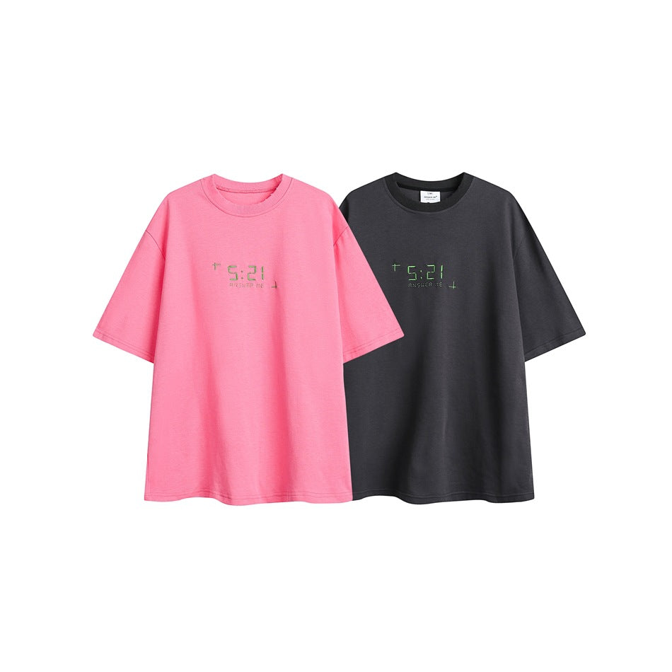 Two oversized T-shirts shown side by side in bright pink and charcoal gray, each with small green chest lettering.