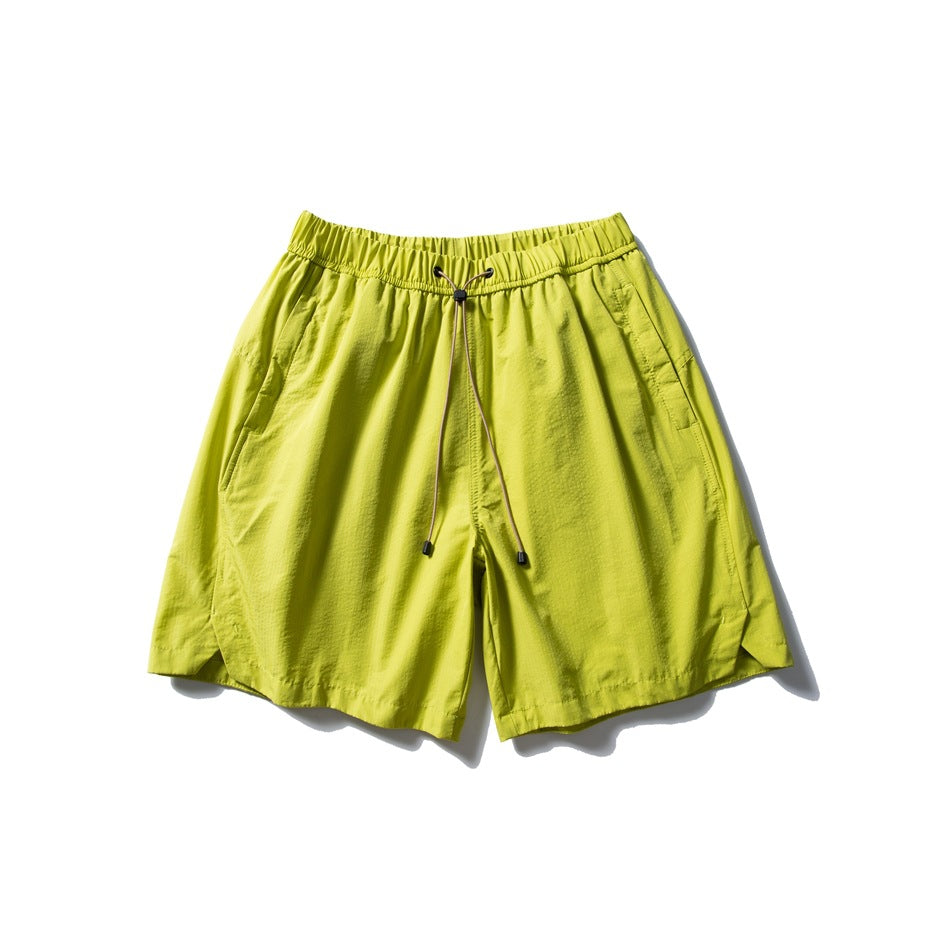 Lime green drawstring shorts with elastic waistband, side pockets and curved side-slit hems, flat lay