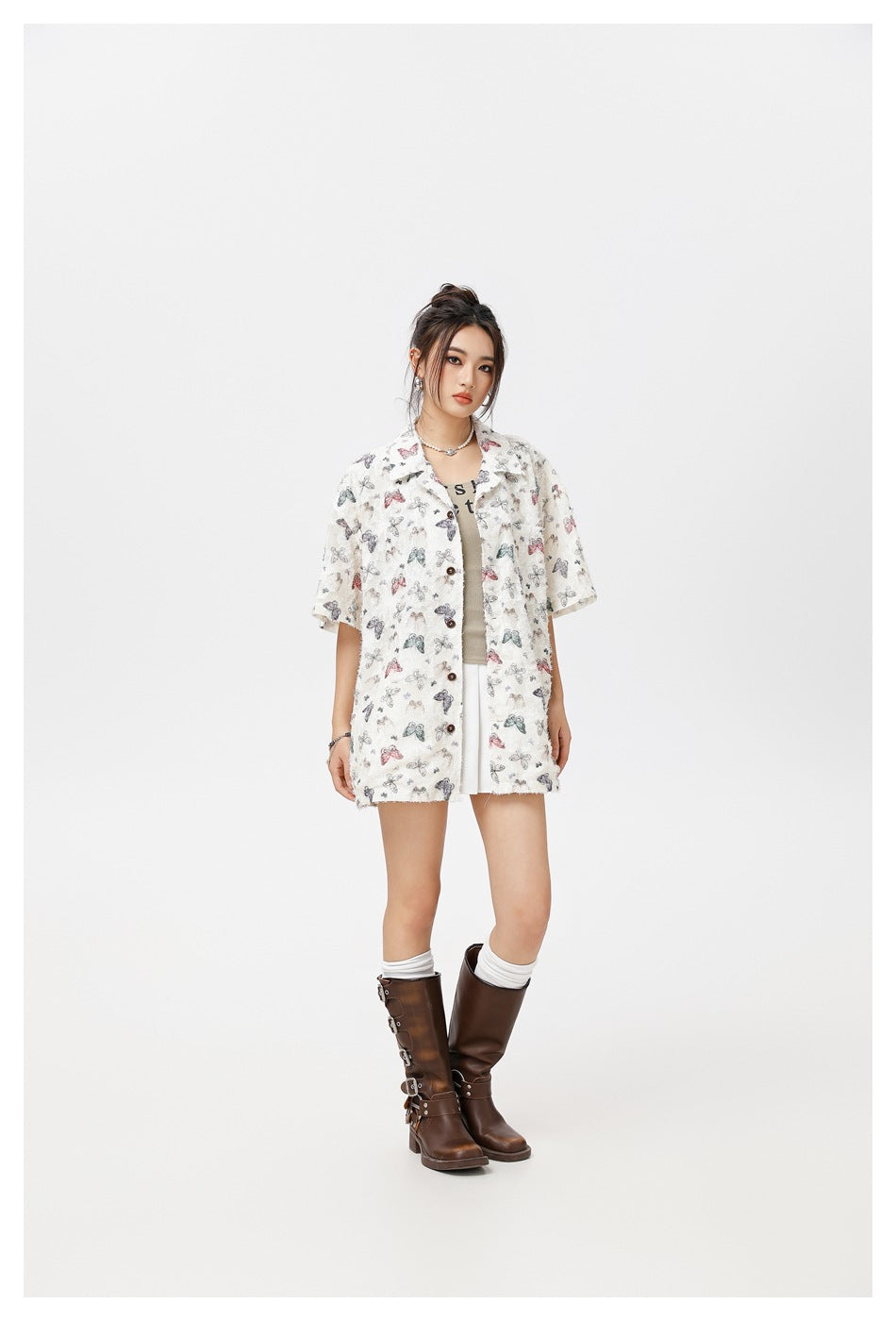 Model in the off-white butterfly print shirt, three-quarter view, with a tank top, white skirt and brown buckle boots