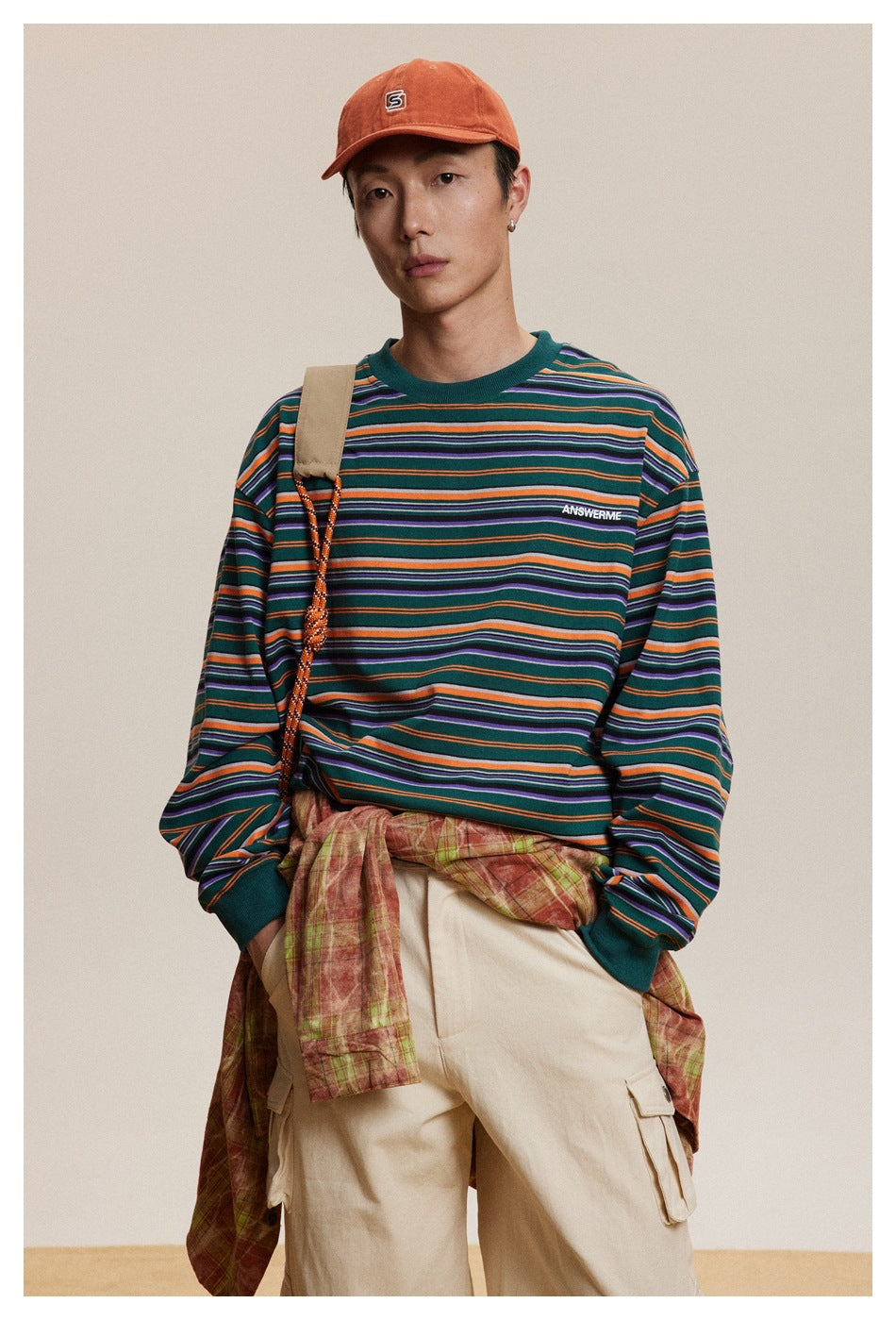 Front view of a model wearing a teal multicolor striped long-sleeve shirt with beige cargo pants and an orange cap.