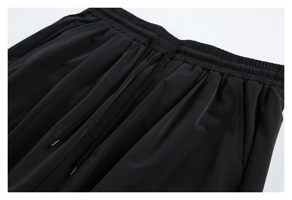 Close-up of black trousers with an elastic waistband, pleats, and two drawstrings.