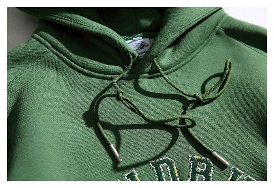 Close-up of the green hoodie’s neckline and knotted drawstrings, with part of its embroidered lettering visible.