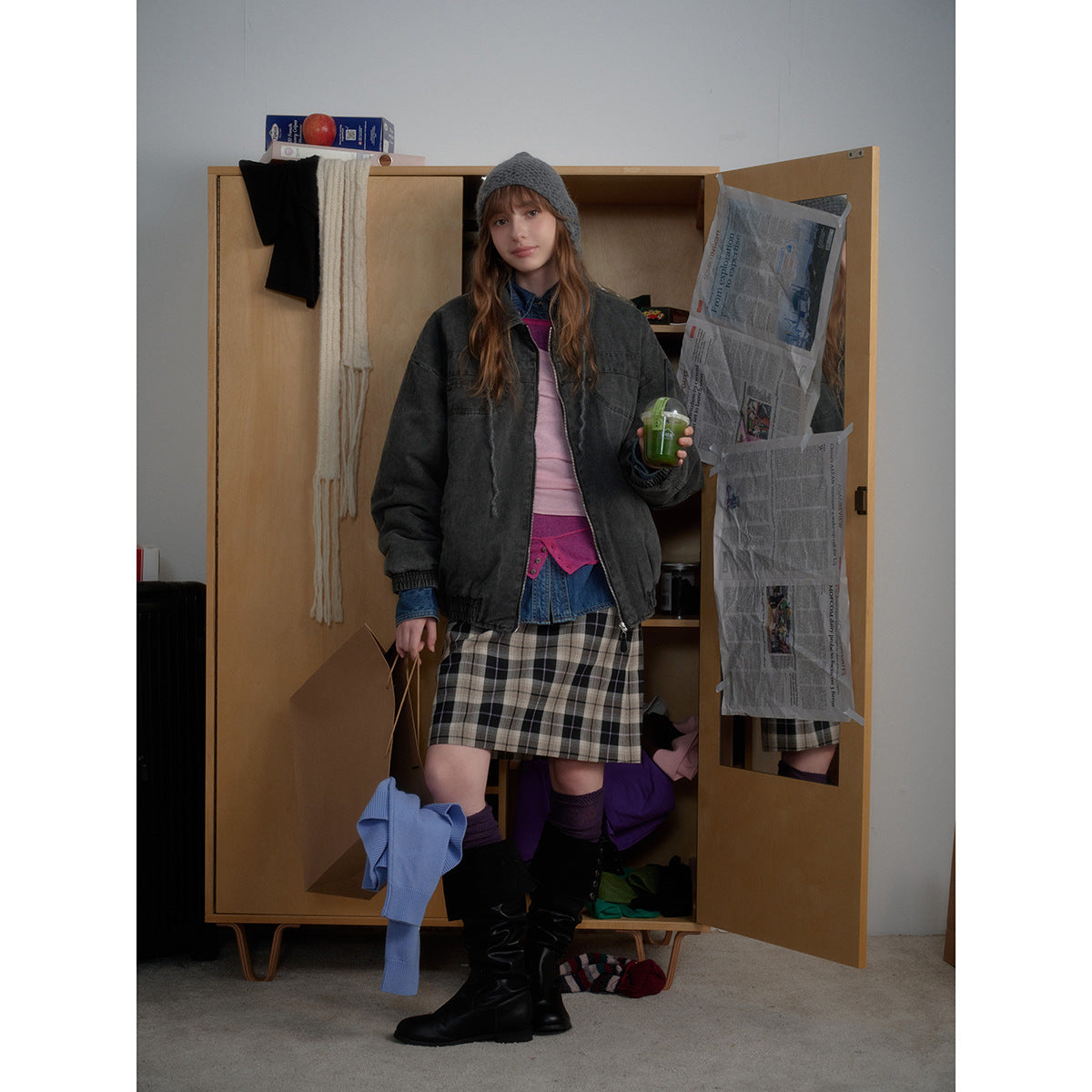 Model wearing a charcoal zip-front jacket over layered tops and a black-and-gray plaid skirt.