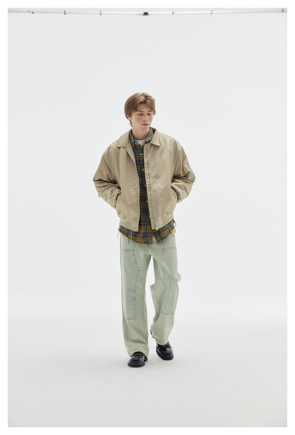 Full-length model wearing a beige zip-front jacket over a plaid shirt with pale green wide-leg jeans.