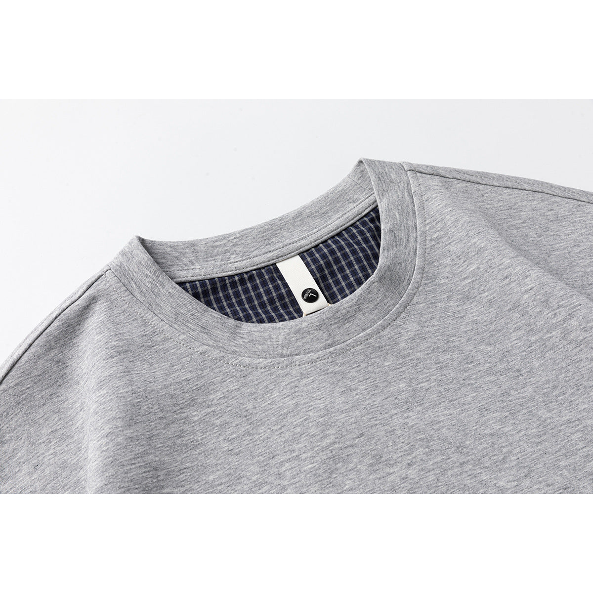 Close-up of a gray crew-neck T-shirt showing its collar and dark plaid inner neck trim.