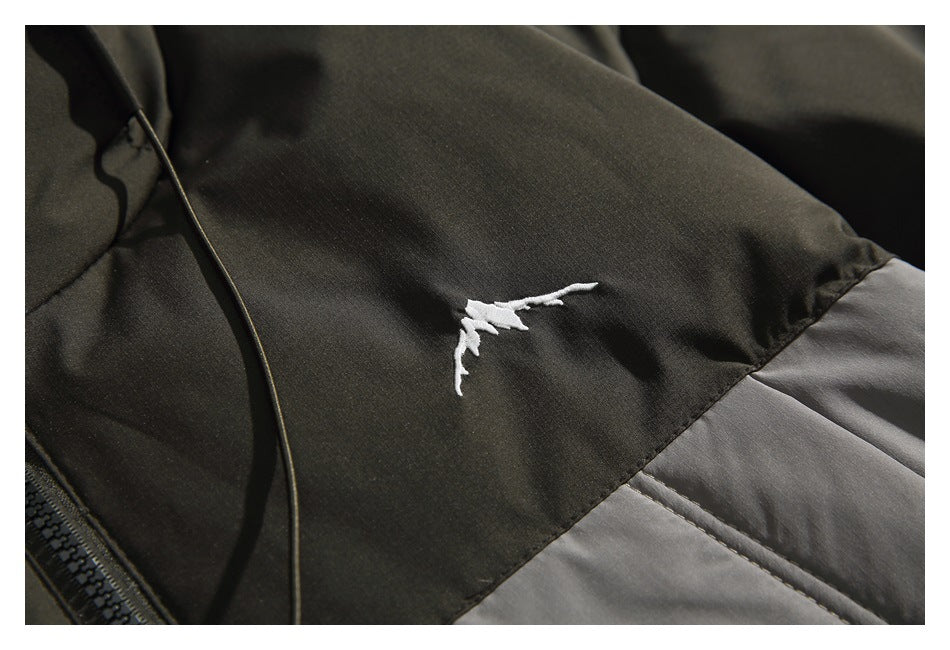Close-up of a small white embroidered emblem on a dark jacket panel above a gray section.