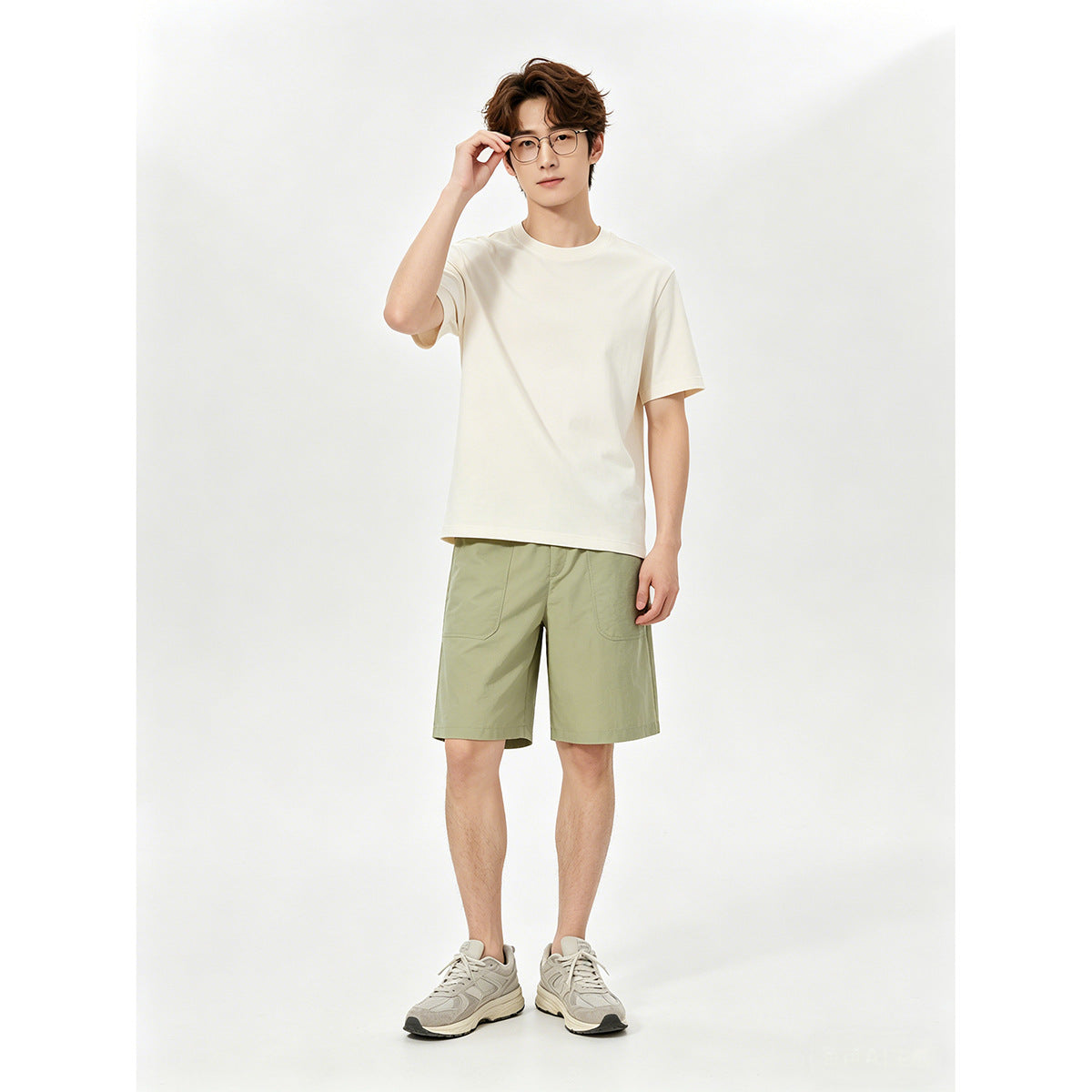 Model wearing an ivory T-shirt with light olive shorts and gray sneakers.
