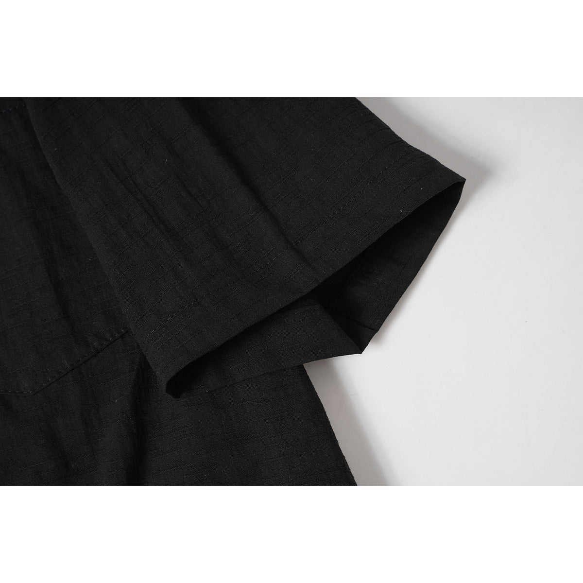 Close-up of the black shirt's short sleeve and hem, showing its subtle woven texture.