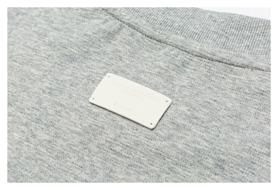 Close-up of a small pale rectangular plaque attached to gray marl knit fabric.