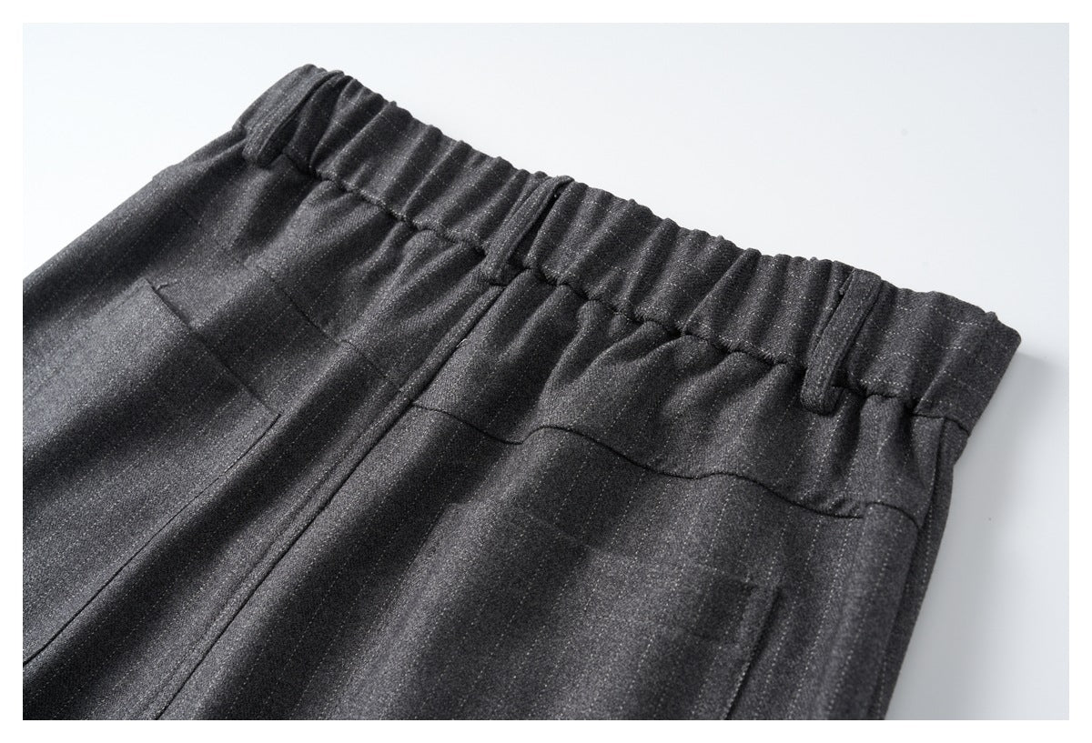 Close-up of charcoal trousers showing an elastic waistband, belt loops, and stitched front seams.