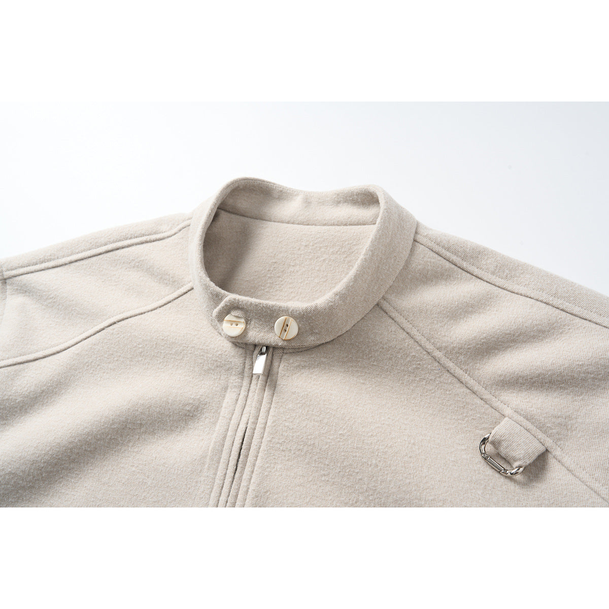 Close-up of a light beige jacket collar with two buttons, front zipper, stitched seams, and a metal shoulder tab.