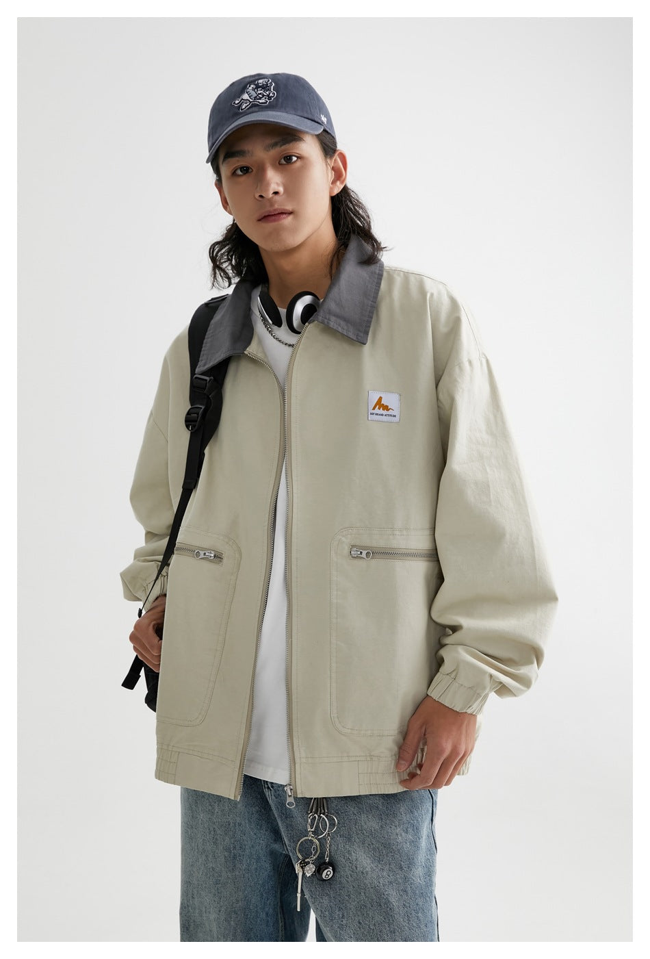 Model wearing a light khaki zip jacket with a contrasting gray collar and two large front pockets.