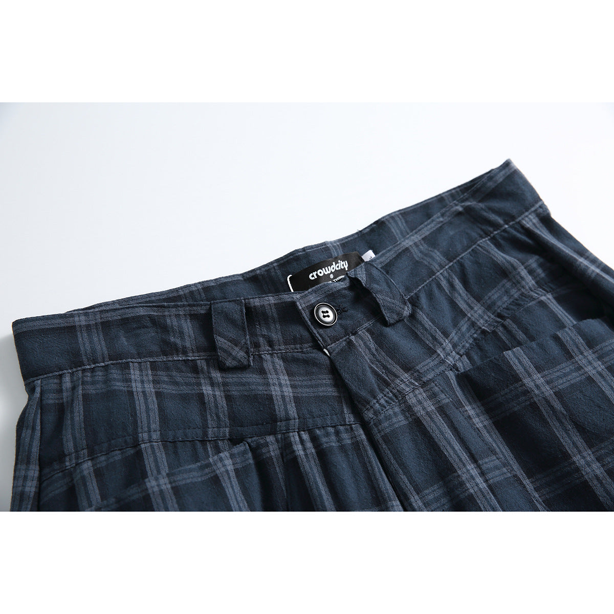 Close-up of navy plaid shorts showing the waistband, button, belt loops, and sewn-in brand label.