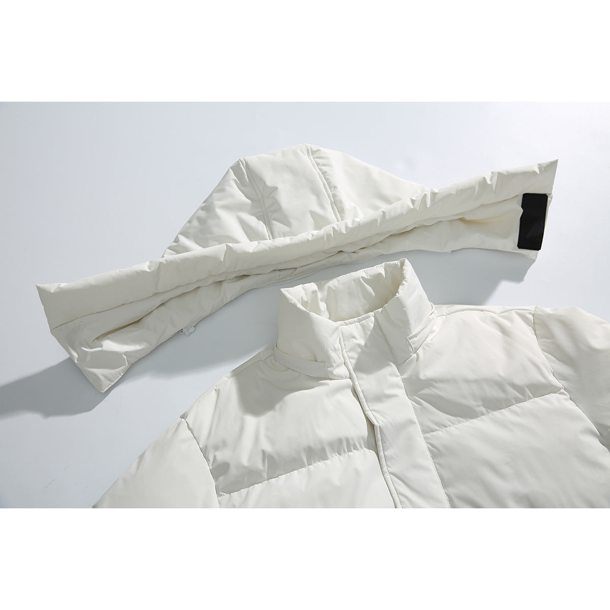 Close-up of an ivory quilted coat showing its high collar, front placket, and sleeve with a black tab.