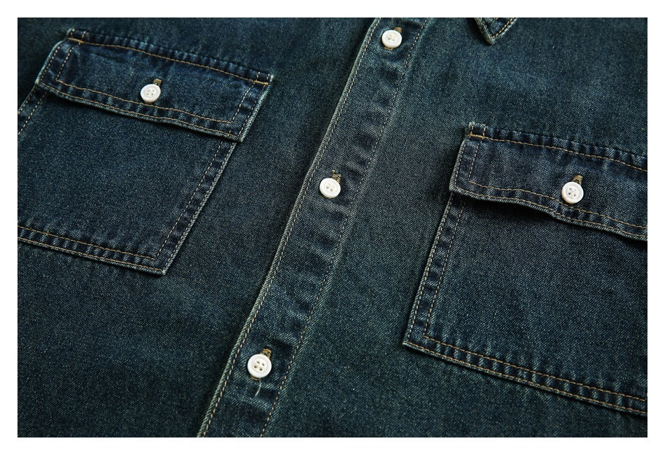 Close-up of the dark indigo denim shirt front, showing two button-flap chest pockets and white buttons.