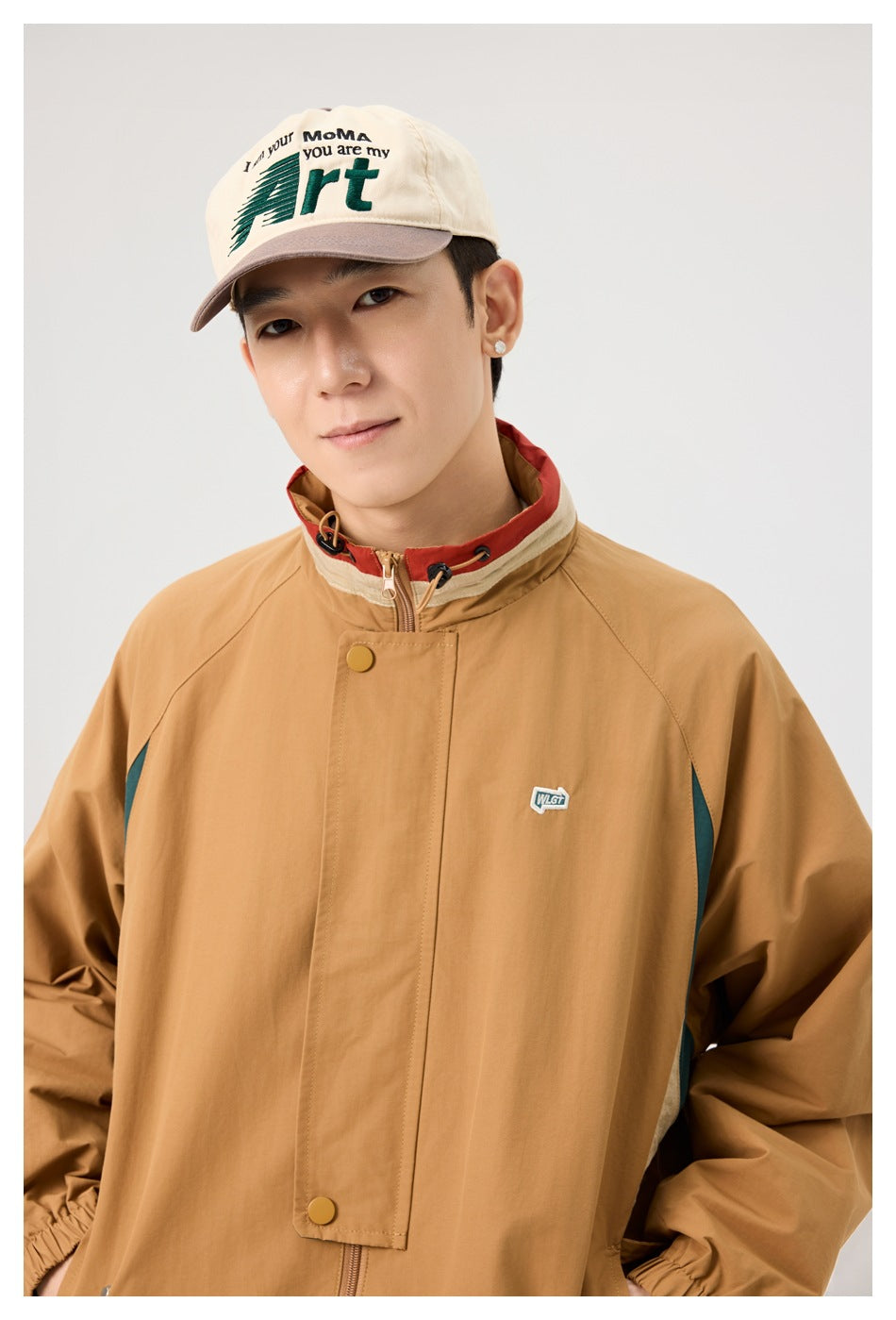 Close view of a model in a tan jacket, showing its stand collar, snap-front flap, and small chest patch.