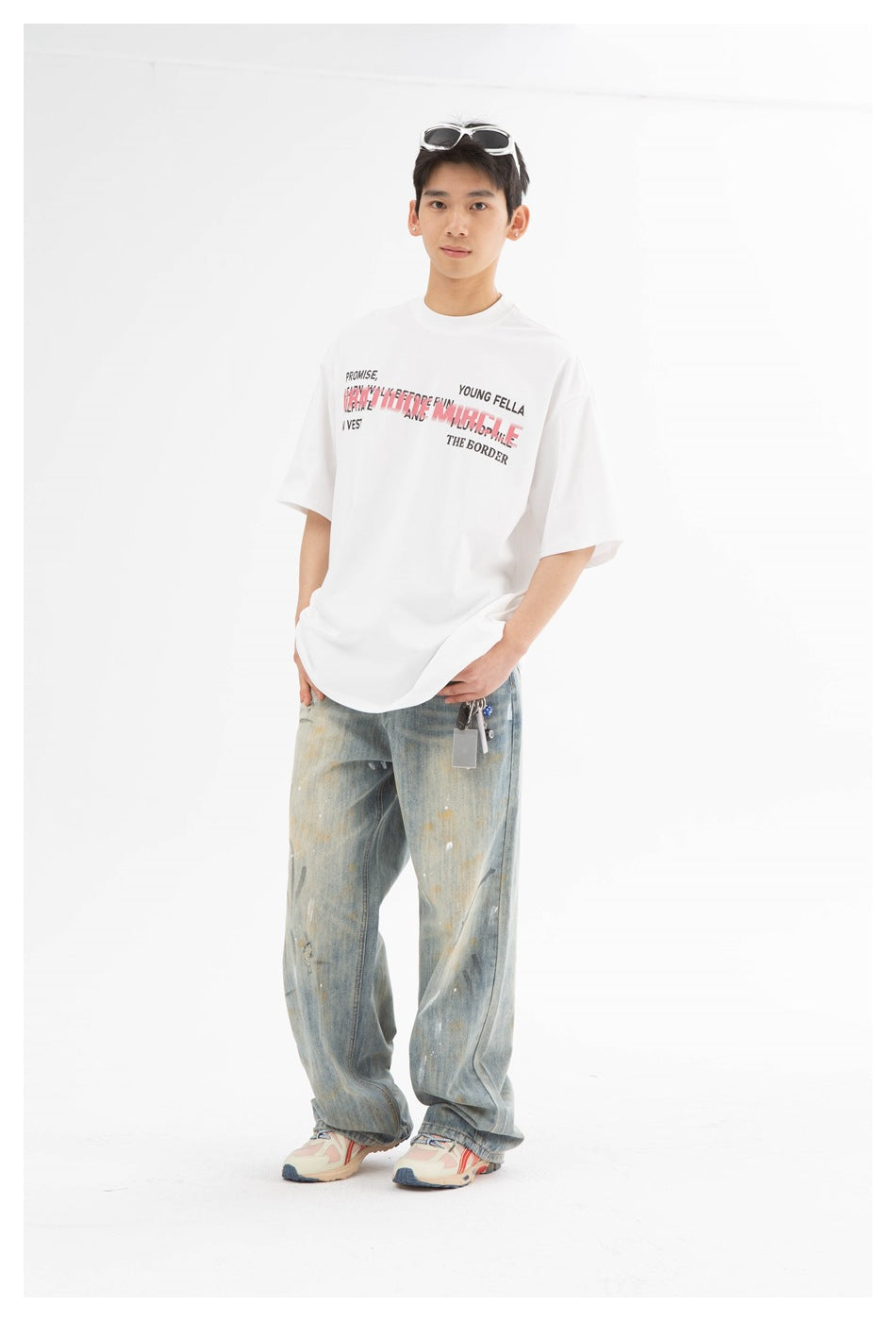 Model in a white text-print T-shirt and loose faded jeans, standing against a white studio background.