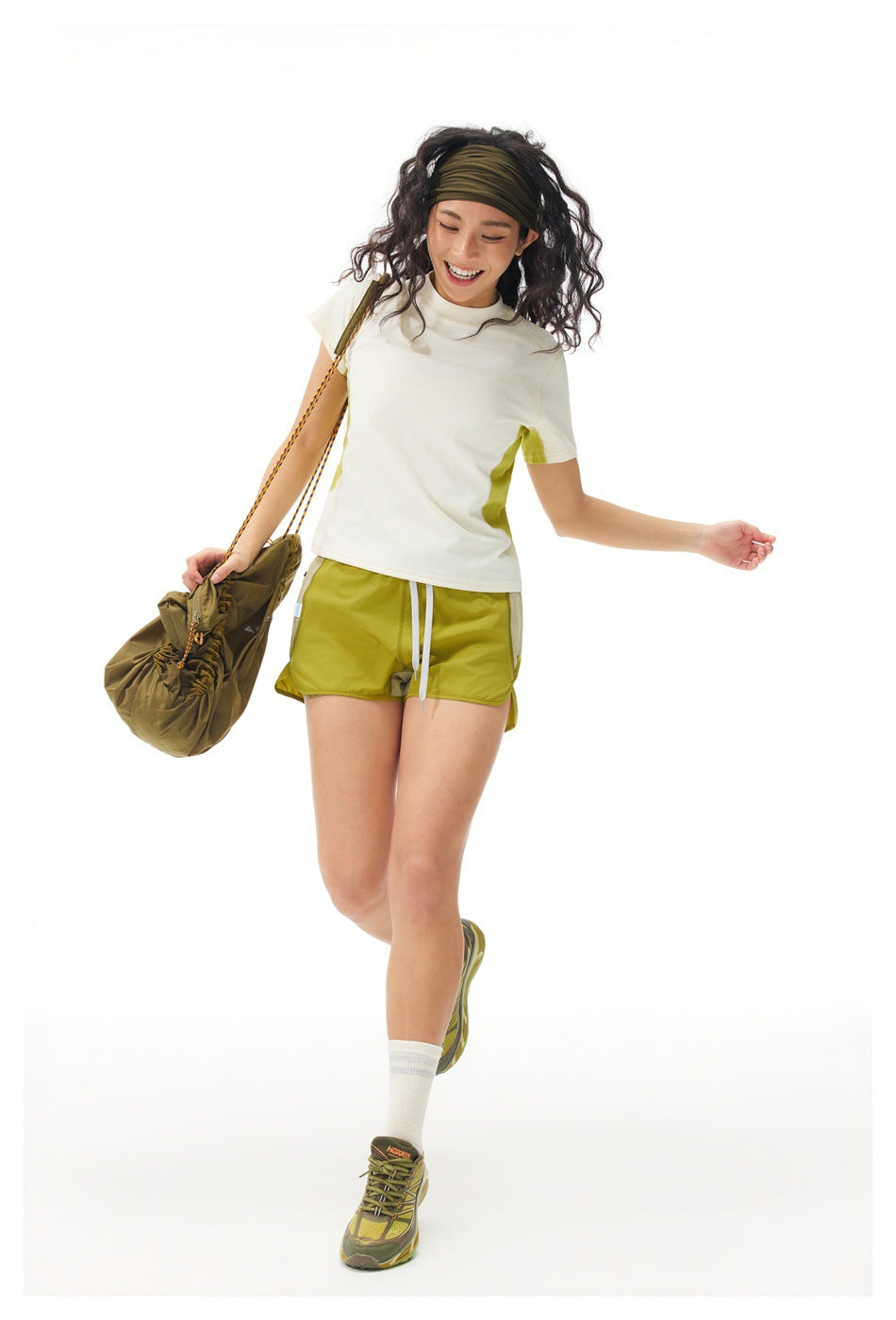 Model wearing a cream T-shirt with lime side panels and lime shorts, carrying a brown bag.