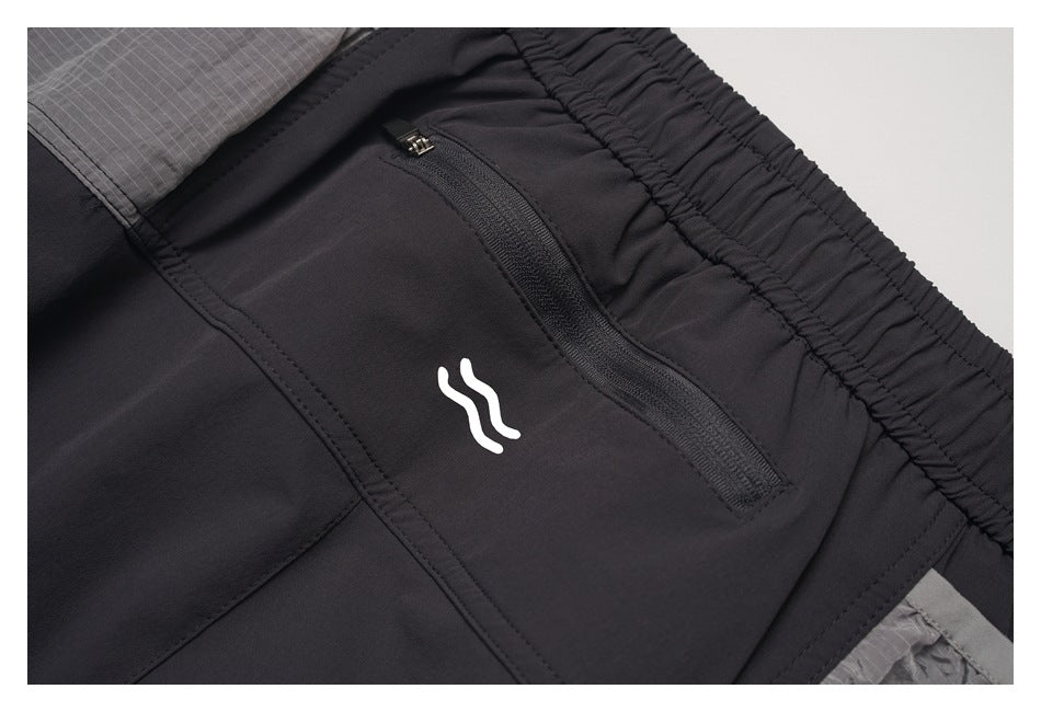 Close-up of a black zippered pocket, white logo and elastic waistband on black pants.