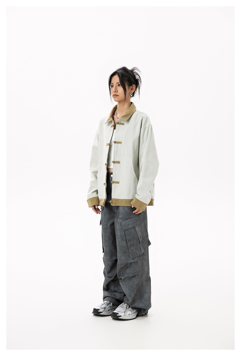 Woman wearing the grey-green frog-button jacket with khaki trim over a white top and grey cargo pants, side view