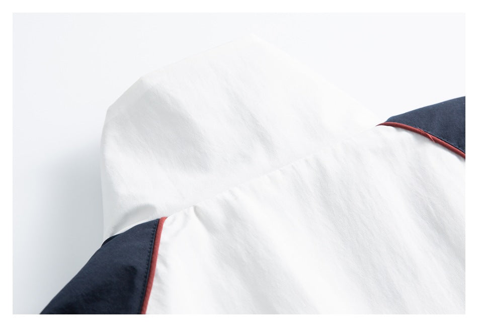 Close-up of white garment fabric with navy panels and thin red piping.