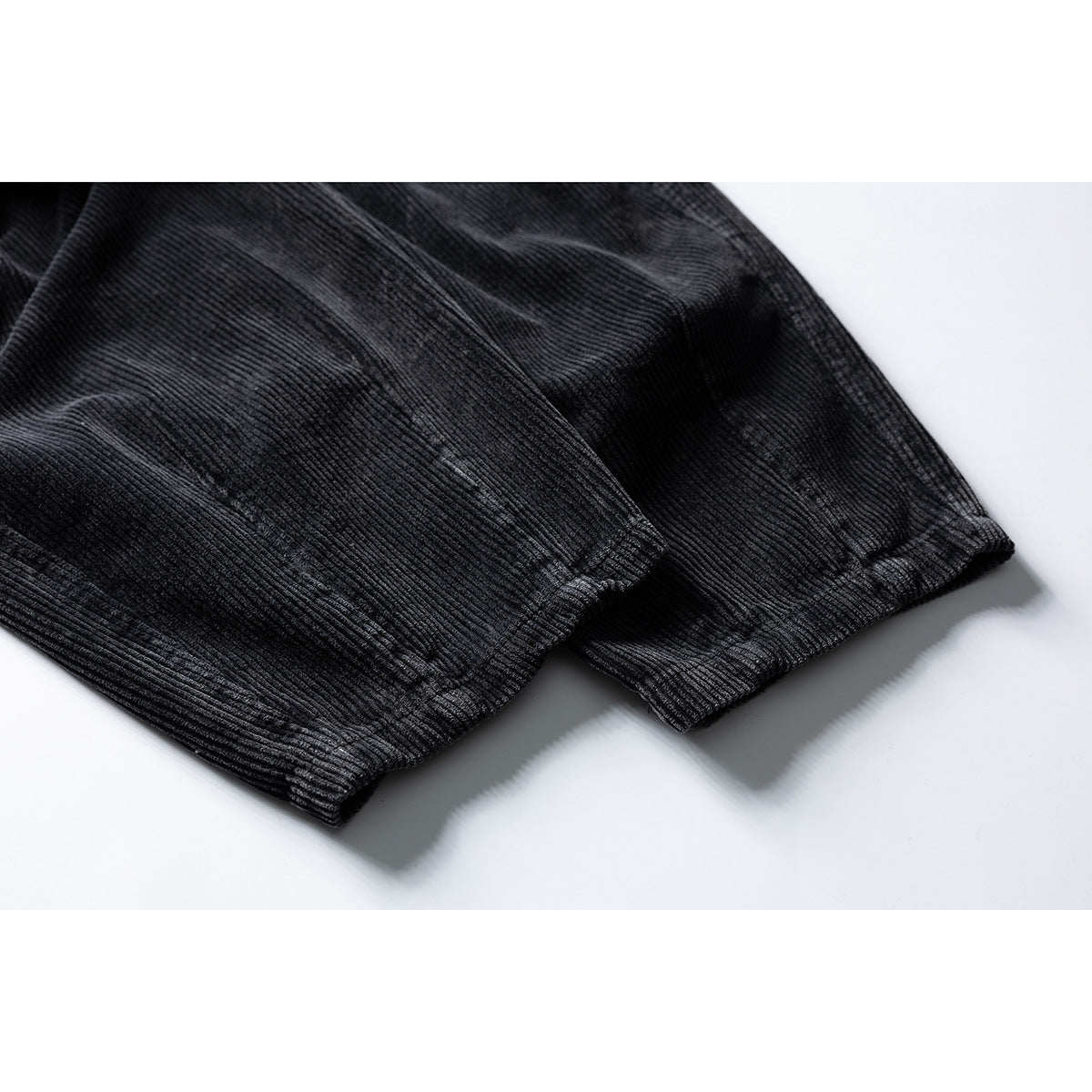 Close-up of the ribbed leg openings on black trousers, laid flat.