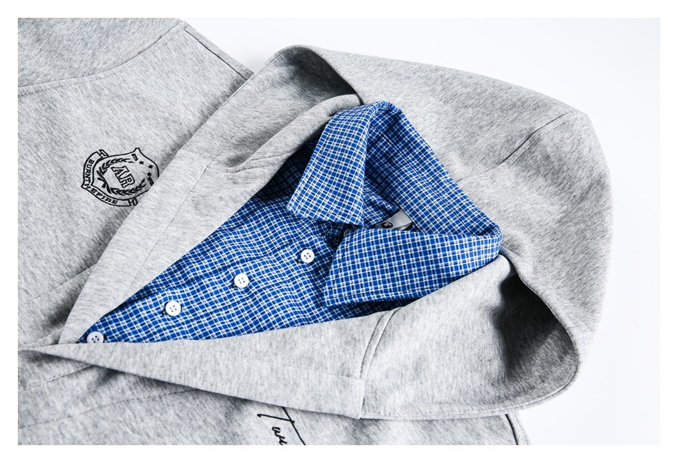 Gray garment layered around a blue-and-white plaid button-up shirt, showing the collar, buttons, and chest emblem.