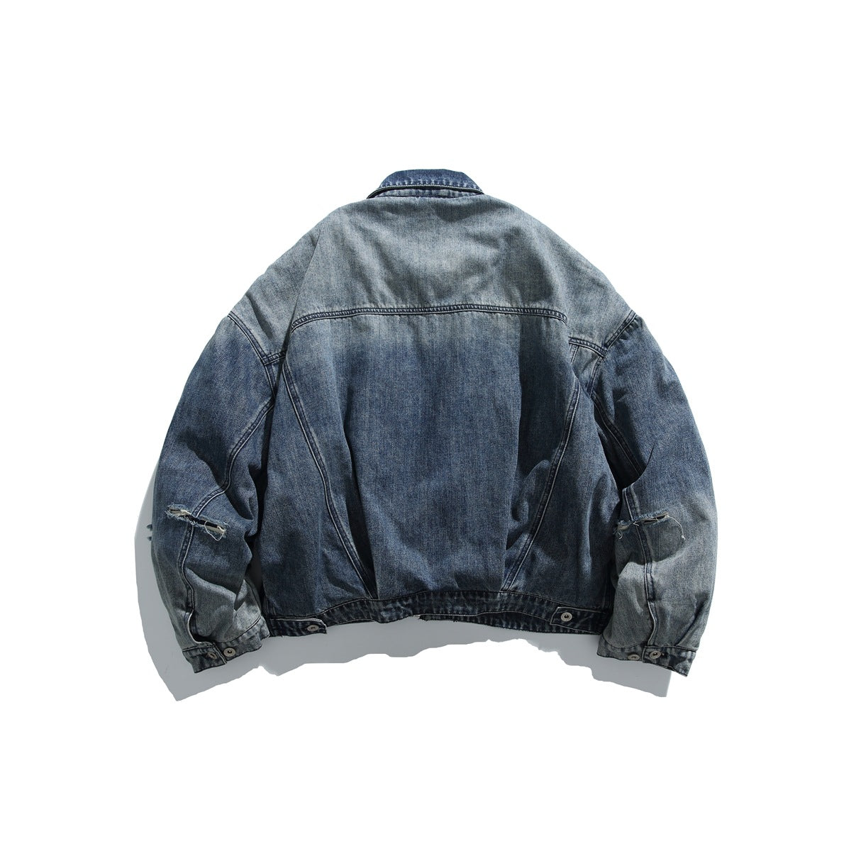 Back view of a blue denim jacket with faded panels, seam detailing and distressed openings on the sleeves.