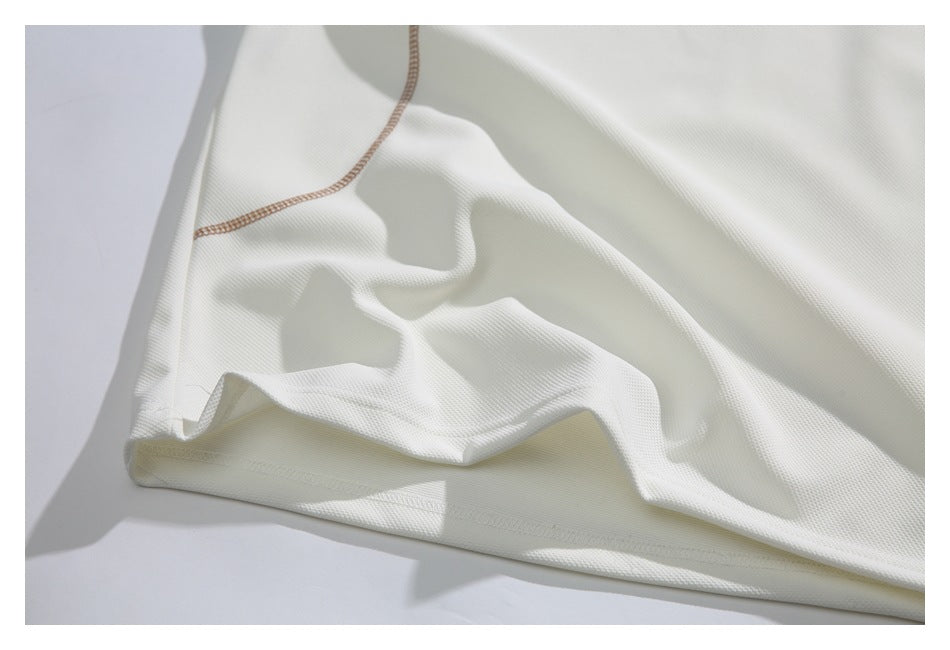 Close-up of white textured garment fabric with a folded hem and contrasting tan stitching.